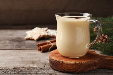 Photo of Glass of delicious eggnog on wooden table, space for text