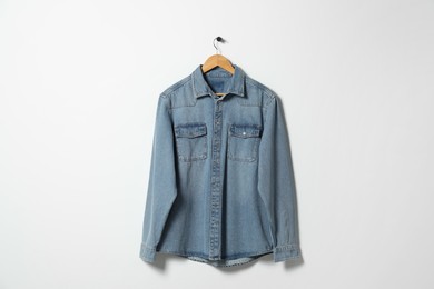 Hanger with denim shirt on white wall