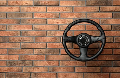Photo of New black steering wheel near red brick wall, space for text