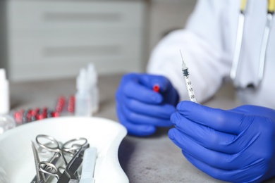 Photo of Doctor holding syringe at table, closeup with space for text. Medical objects