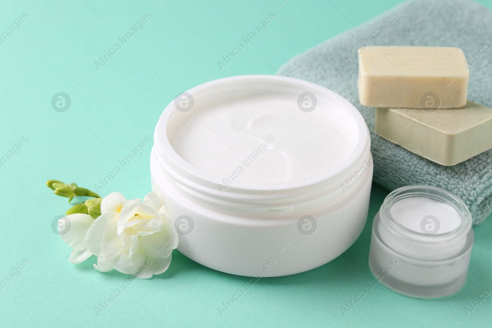 Photo of Moisturizing cream in open jars, soap bars and freesia flower on turquoise background. Body care products