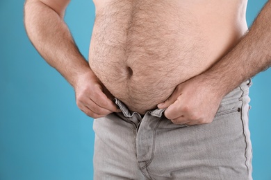 Photo of Overweight man trying to button jeans on color background, closeup