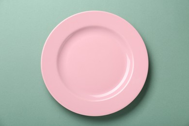 Empty pink ceramic plate on green background, top view