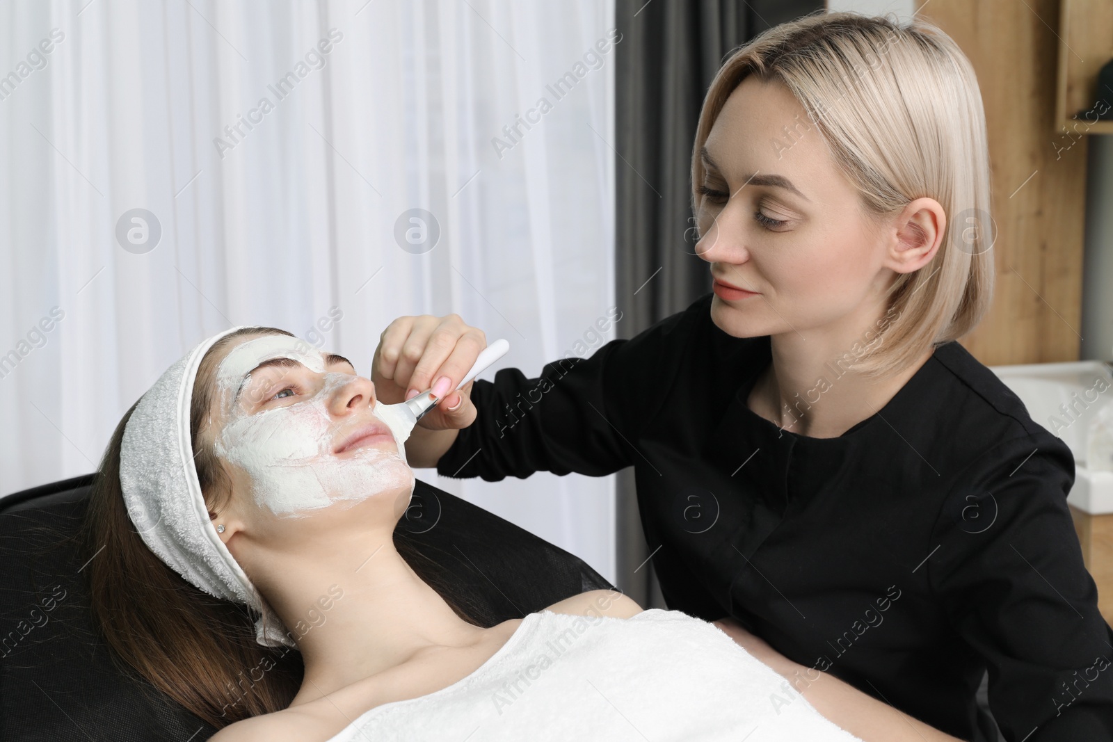 Photo of Cosmetologist applying mask on woman's face in clinic