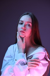 Fashionable portrait of beautiful young woman on purple background in neon lights