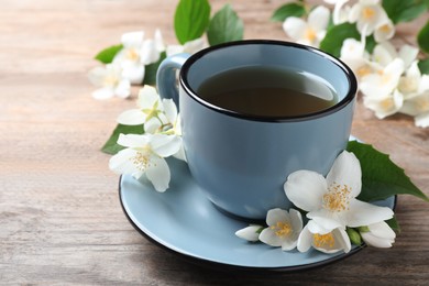 Photo of Cup of tea and fresh jasmine flowers on wooden table