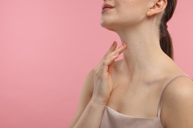 Woman touching her neck on pink background, closeup. Space for text