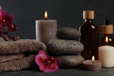 Photo of Beautiful composition with burning candles, spa stones and different care products on dark grey table, closeup