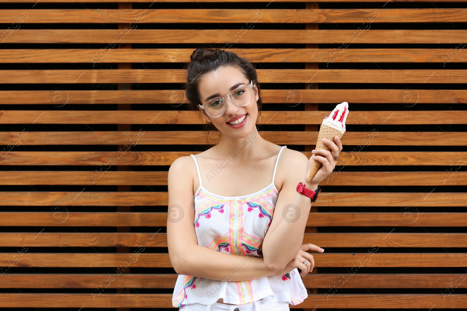 Photo of Happy young woman with delicious ice cream in waffle cone near wooden wall