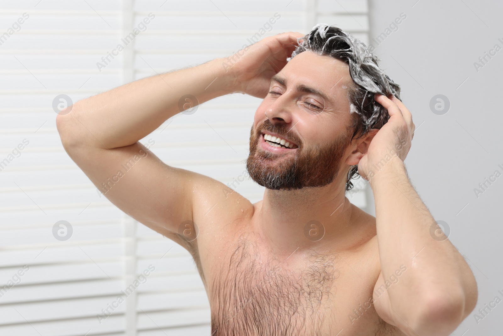 Photo of Happy man washing his hair with shampoo in shower