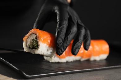 Chef in gloves making sushi rolls at grey table, closeup