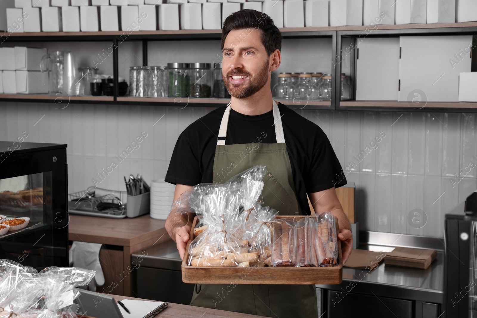 Photo of Happy seller with pastries at cashier desk in bakery shop