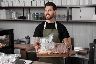 Happy seller with pastries at cashier desk in bakery shop