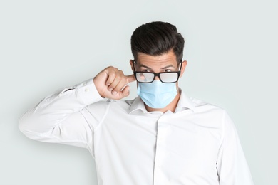 Photo of Man wiping foggy glasses caused by wearing medical mask on light background