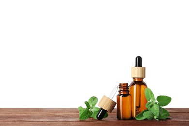 Bottles of essential oil and mint on wooden table against white background