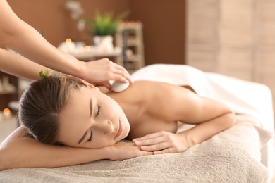 Photo of Young woman having traditional hot stones massage in spa salon