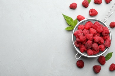 Strainer with delicious ripe raspberries on light background, top view. Space for text