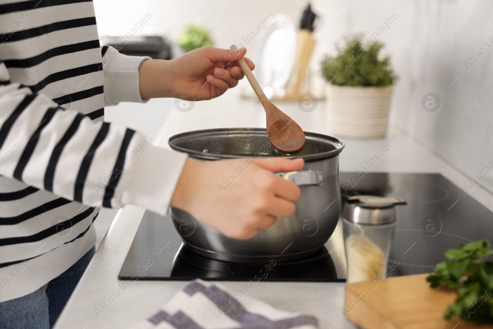 Photo of Woman with wooden spoon cooking soup in kitchen, closeup