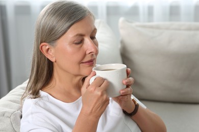 Photo of Senior woman with cup of tea on sofa at home