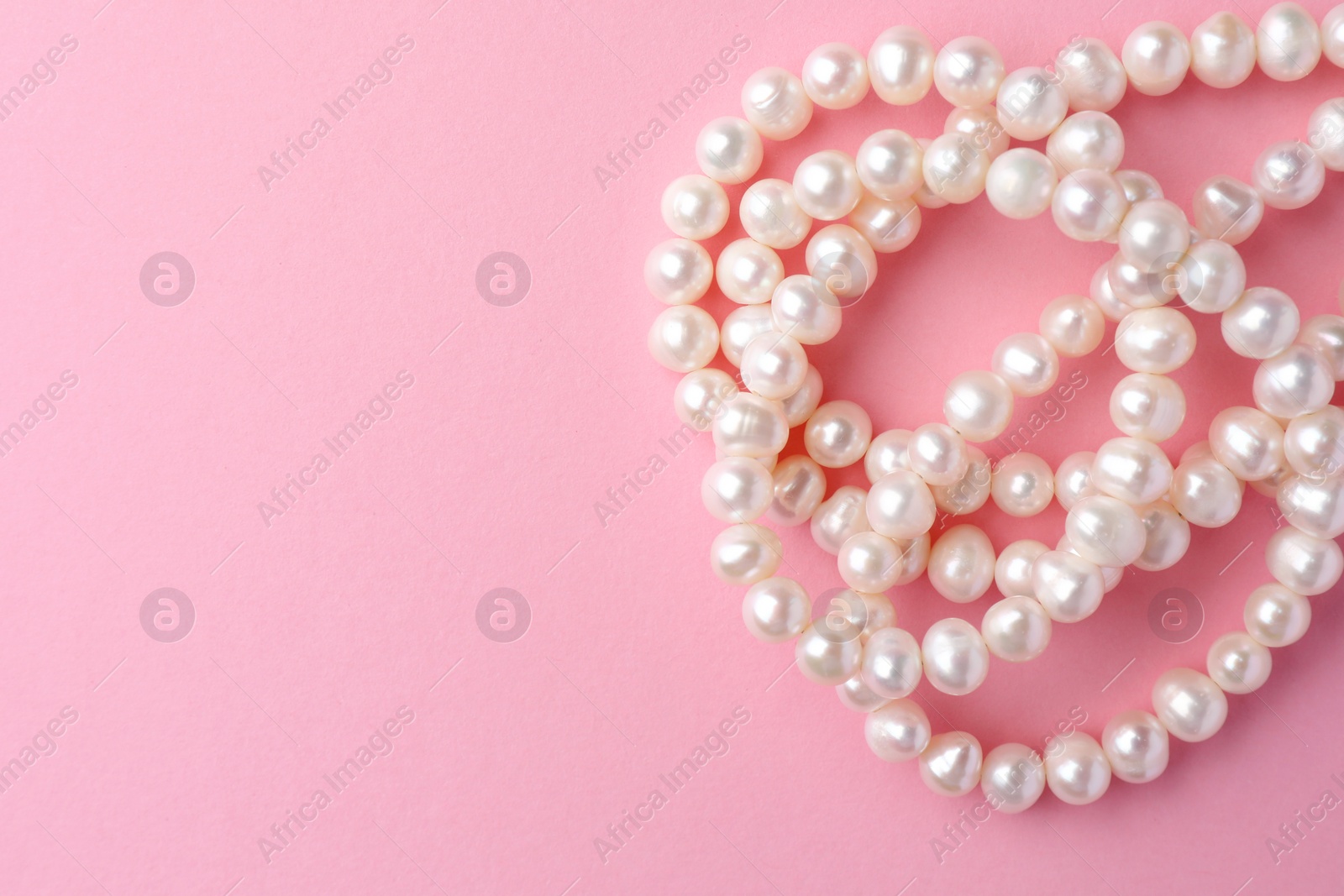 Photo of Elegant necklace with pearls on pink background, top view. Space for text
