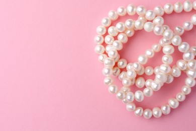 Elegant necklace with pearls on pink background, top view. Space for text
