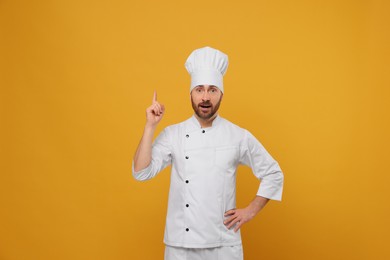 Photo of Mature male chef showing idea gesture on orange background