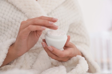 Photo of Woman holding jar with cream on light background, closeup