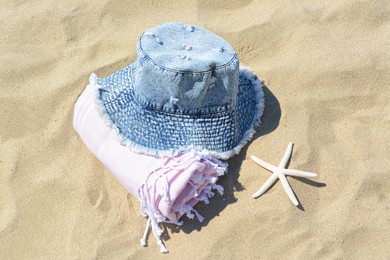 Stylish denim hat, blanket and starfish on sand outdoors, above view. Beach accessories