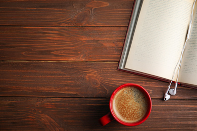 Photo of Open book, earphones and coffee on wooden table, flat lay. Space for text