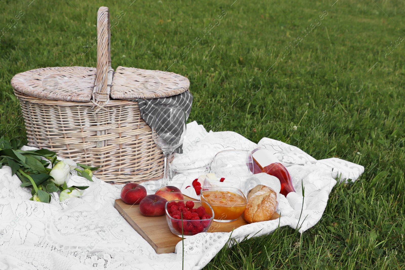 Photo of Picnic blanket with tasty food, flowers, basket and cider on green grass outdoors. Space for text