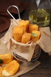 Photo of Metal basket with tasty fried mozzarella sticks on wooden table