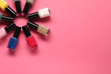 Photo of Bright nail polishes in bottles on pink background, flat lay. Space for text