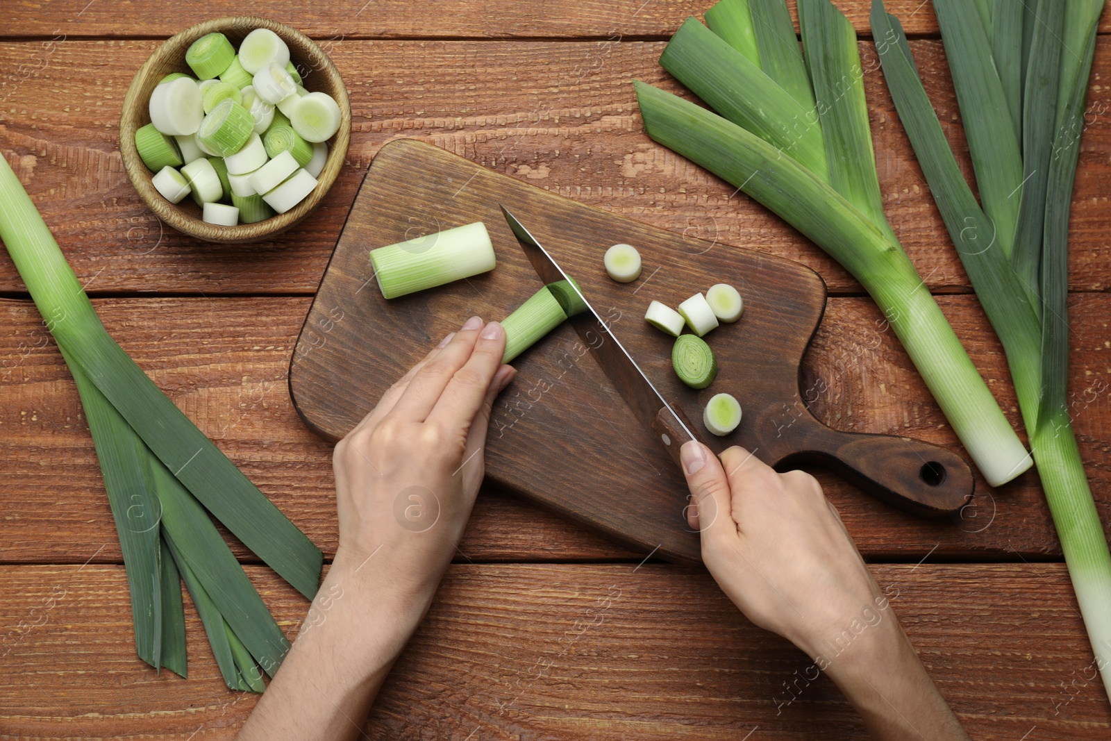 Photo of Woman cutting fresh raw leek at wooden table, top view