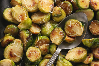 Delicious roasted brussels sprouts with grated cheese and spoon as background, closeup