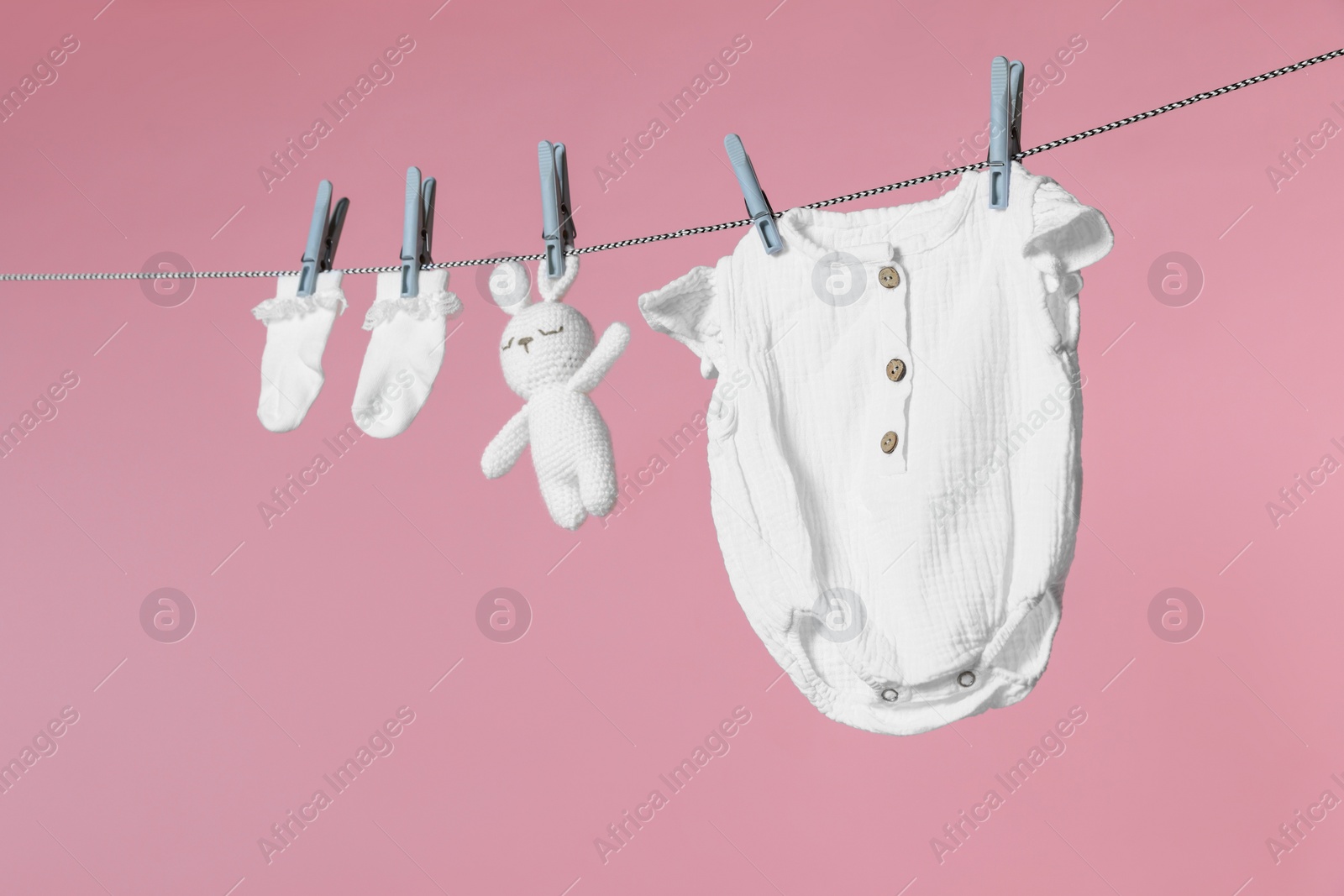 Photo of Different baby clothes and bunny toy drying on laundry line against pink background