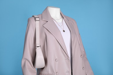 Photo of Female mannequin dressed in white t-shirt and stylish leather jacket with accessories on light blue background