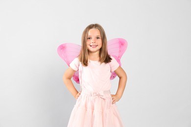 Photo of Cute little girl in fairy costume with pink wings on light background