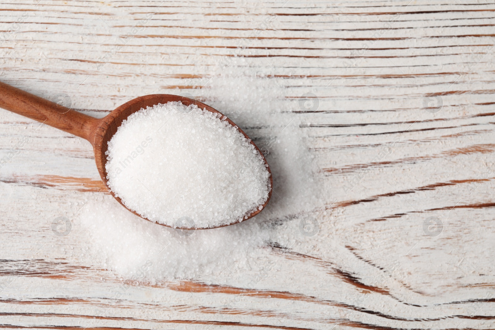 Photo of Spoon and granulated sugar on white wooden table, top view. Space for text