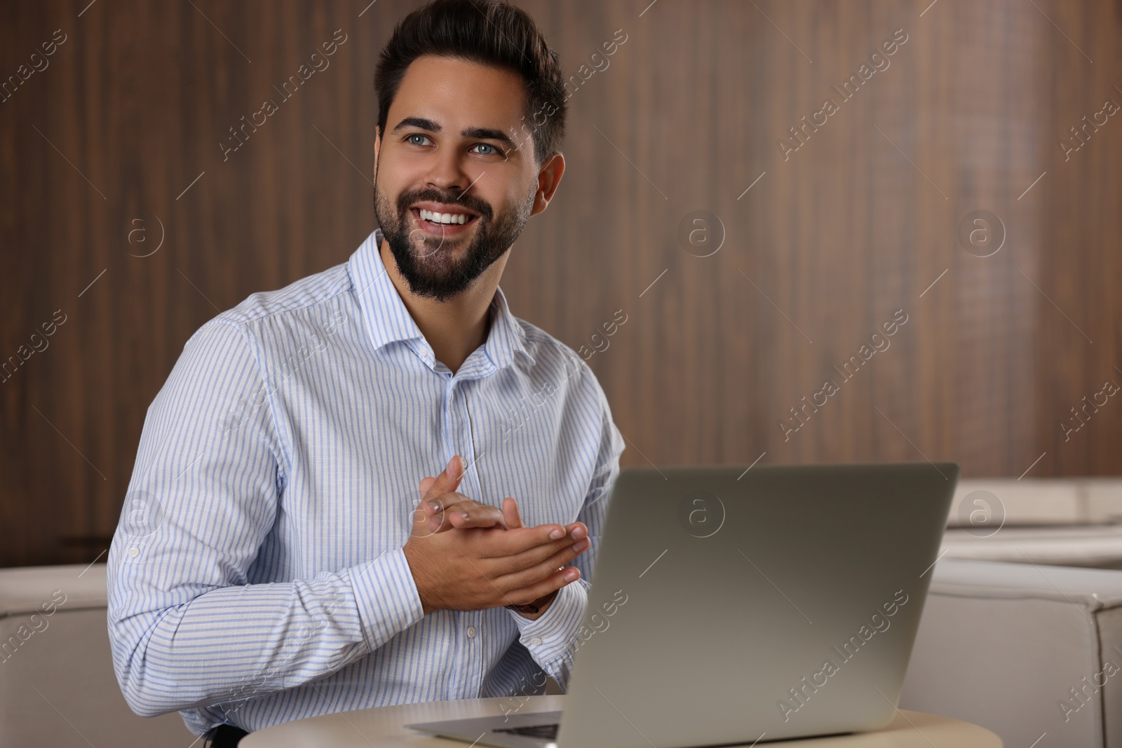 Photo of Happy young man with laptop at table in office