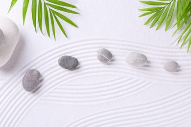 Photo of Zen garden stones and green leaves on white sand with pattern, flat lay