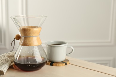 Glass chemex coffeemaker with coffee and cup on table, space for text
