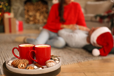 Photo of Happy couple on floor in room, focus on tray with cups. Christmas celebration