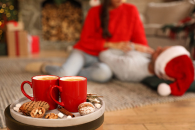 Happy couple on floor in room, focus on tray with cups. Christmas celebration