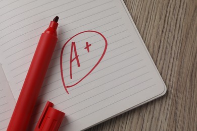 School grade. Red letter A with plus symbol on notebook paper and marker on wooden table, top view