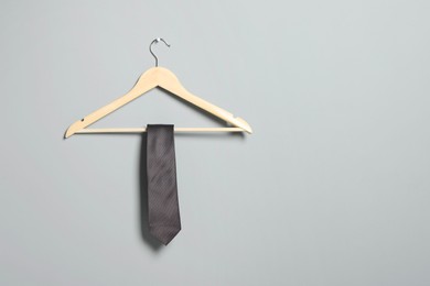 Hanger with necktie on light grey wall. Space for text