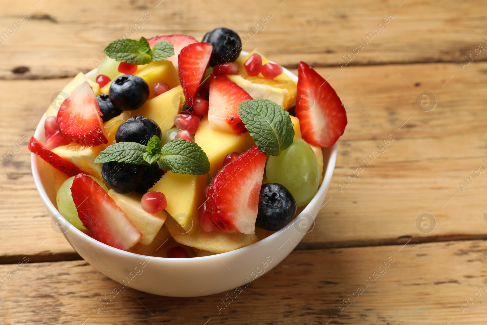 Photo of Tasty fruit salad in bowl on wooden table, closeup