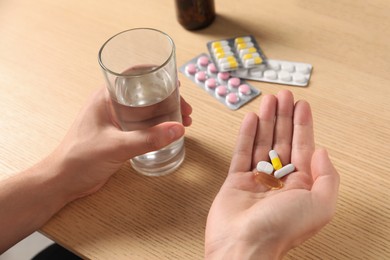 Man with glass of water and pills at wooden table, closeup