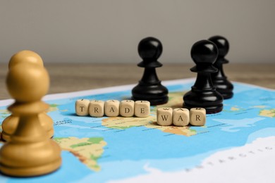 Photo of Phrase Trade war made with cubes, chess pieces and world map on wooden table, closeup