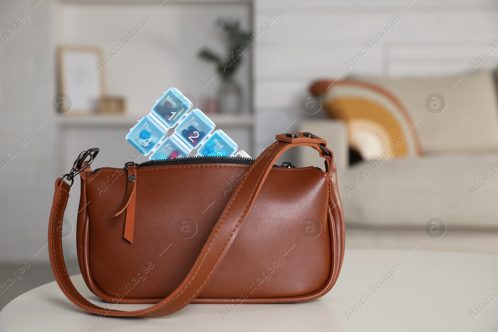 Photo of Stylish women's bag with plastic pill box on white table in room. Space for text