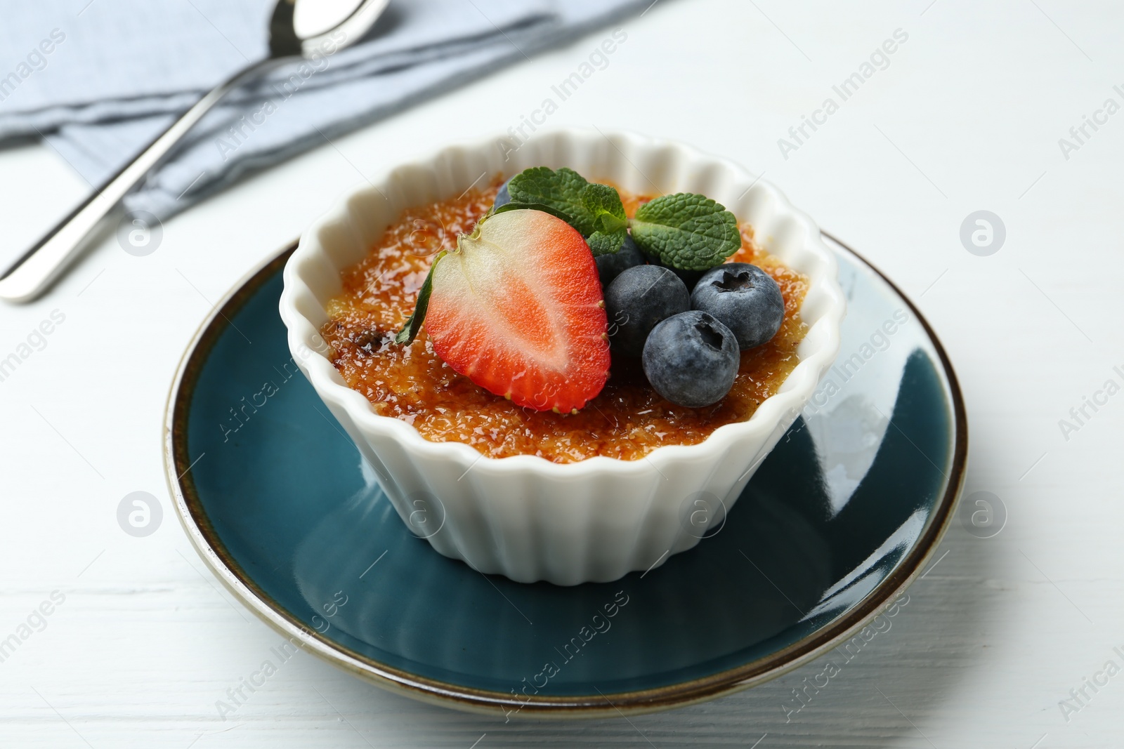 Photo of Delicious creme brulee with berries and mint in bowl on white wooden table, closeup